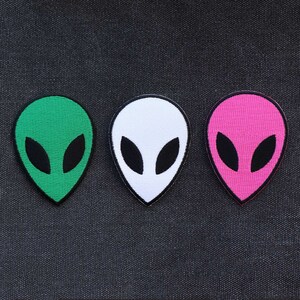 May include: Three alien head patches in green, white, and pink. Each patch has a black outline and black eyes.