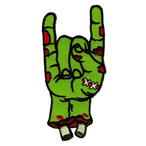 Op de afbeelding: Geborduurde patch met een groene zombiehand die het rock and roll-gebaar maakt. De hand heeft rode bloedvlekken, hechtingen en blootliggend bot bij de pols. Zwarte omtrek.