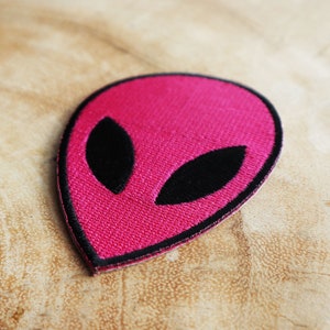 May include: A pink alien face embroidered patch with black eyes.