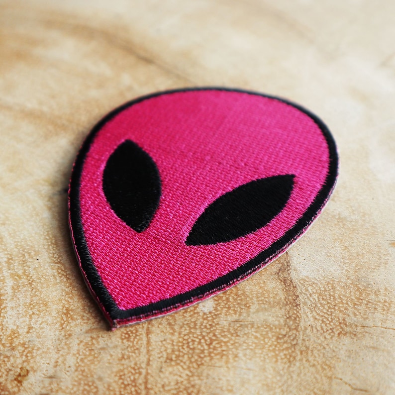 May include: A pink alien face embroidered patch with black eyes.