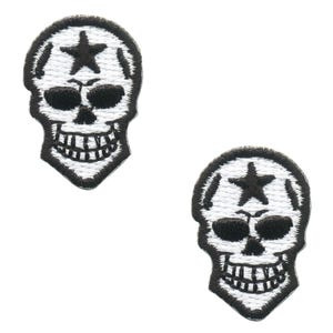 May include: Two embroidered patches featuring a skull design with a star on the forehead. The patches are white with black detailing, including the skull's eyes, nose, and teeth. The patches are likely for clothing or accessories.