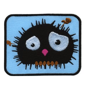 Pode incluir: Um remendo bordado em preto e branco de uma criatura de desenho animado com um corpo espinhoso, grandes olhos azuis e um nariz rosa. A criatura está sobre um fundo azul claro.