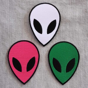 May include: Three alien head patches in different colours: white, pink, and green. Each patch has a black outline and black eyes.