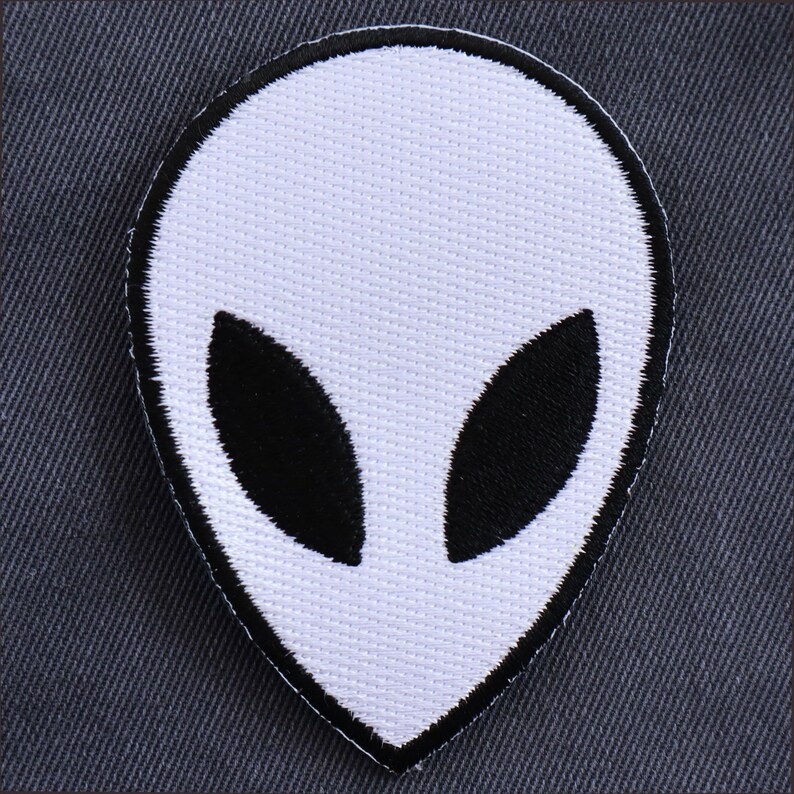 May include: White alien head patch with black eyes. The patch is made of fabric and has a stitched outline.