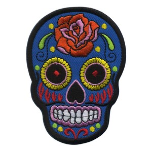 Könnte beinhalten: Gestickter blauer Zucker Schädel Patch mit einer roten Rose, gelben und grünen Blumendetails und schwarzen Augen.