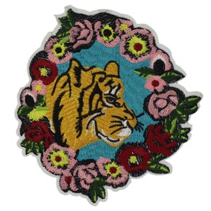 May include: Embroidered iron-on patch featuring a tiger's head surrounded by a colorful floral wreath. The tiger is orange and black with a blue background. The flowers are pink, red, yellow, and green.