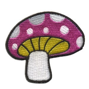 Op de afbeelding: Gestikt pleister van een roze paddenstoel met witte stippen en een gele dop. De paddenstoel heeft een witte steel.
