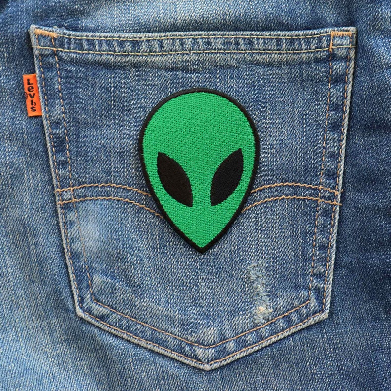 May include: Green alien face patch on a blue denim pocket.
