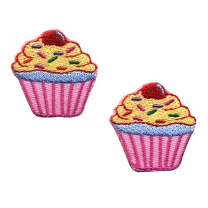 Könnte beinhalten: Zwei gestickte Cupcake-Aufnäher in Rosa und Gelb mit einer roten Kirsche oben. Die Cupcakes haben blauen Zuckerguss und bunte Streusel.