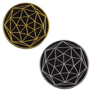 Könnte beinhalten: Zwei runde, gestickte Aufnäher. Einer zeigt ein goldenes geometrisches Design auf schwarzem Hintergrund. Der andere hat ein silbernes geometrisches Design auf schwarzem Hintergrund. Die Aufnäher sind wahrscheinlich für Kleidung oder Accessoires.