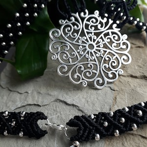 May include: A black cord necklace with a silver filigree pendant. The cord is made of braided black thread with silver beads.