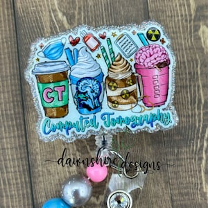 May include: A blue and white glitter badge reel with a design of coffee cups, a brain, and the text "Computed Tomography". The reel has a silver clip and a clear plastic badge holder with three colorful beads.