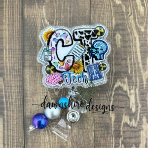 May include: A sparkly white and silver badge reel with a colorful CT Tech design. The design includes a brain, a stethoscope, a sunflower, and an X-ray image. The reel has a clear plastic badge holder and a silver chain with blue and silver beads.