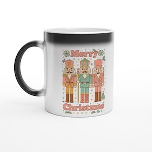 May include: A white ceramic mug with a black handle. The mug has a festive design featuring three nutcracker figures in red, green, and gold, with the words "Merry Christmas" in a retro font. Ideal for seasonal drinks.