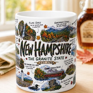 May include: A white ceramic mug featuring a colorful illustrated map of New Hampshire. The design includes landmarks like Flume Gorge, Kancamagus Highway, the State House, Cornish-Windsor Bridge, and Old Man of the Mountain, with the text New Hampshire.