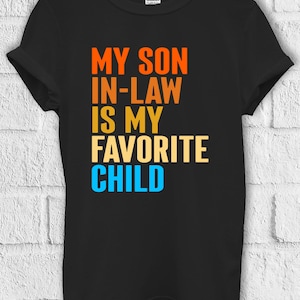 May include: Black t-shirt with the text "My son in-law is my favourite child" in orange, yellow, and blue.