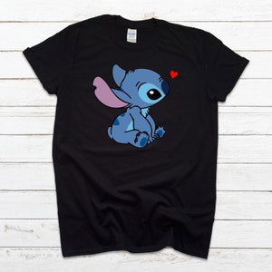 Op de afbeelding: Zwart T-shirt met een blauw Stitch-personage uit Lilo & Stitch. Stitch zit met een roze oor en een rood hart boven zijn hoofd.