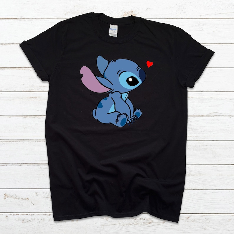Op de afbeelding: Zwart T-shirt met een blauw Stitch-personage uit Lilo & Stitch. Stitch zit met een roze oor en een rood hart boven zijn hoofd.