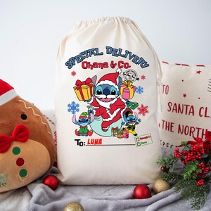 May include: A white canvas gift bag with a blue Stitch character from Lilo & Stitch wearing a Santa hat and holding a gift. The bag has the text "SPECIAL DELIVERY Ohana & Co" and "To: LUNA".