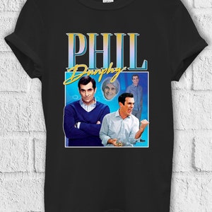 Könnte beinhalten: Schwarzes T-Shirt mit einer Retro-Grafik von Phil Dunphy aus der Fernsehserie Modern Family. Die Grafik zeigt drei Bilder von Phil in verschiedenen Posen, mit dem Text "Phil Dunphy" in goldener Schrift.