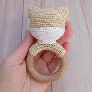 May include: A crocheted beige and white cat head attached to a wooden teething ring.