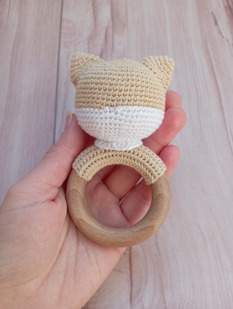 May include: A crocheted beige and white cat head attached to a wooden teething ring.
