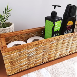 Puede incluir: Una cesta de mimbre con dos rollos de papel higiénico, una botella de champú etiquetada como "Not Only Shampoo" y una botella de solución de limpieza etiquetada como "Konev".