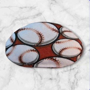 Puede incluir: Una máscara para los ojos marrón y blanca con un patrón de béisbol. La máscara está hecha de tela suave y tiene un ajuste cómodo.