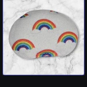 May include: A white plush eye mask with a rainbow pattern. The eye mask is shaped like a bean and has a soft, fuzzy texture.