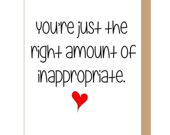 May include: A white greeting card with black text that reads, "you're just the right amount of inappropriate." Below the text is a small, solid red heart. The card is positioned against a plain tan background, showing a portion of the envelope edge.