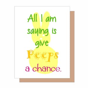 May include: A greeting card with a white background and a brown border. The card features a yellow bunny shape with the words "All I am saying is give Peeps a chance" in green, yellow, and pink.