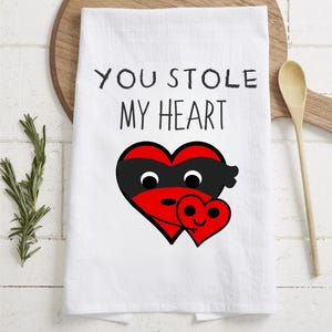 May include: White kitchen towel with the text "You stole my heart" and a red heart with a black mask holding a smaller red heart with a smiley face.