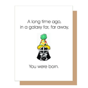 May include: A birthday card featuring Darth Vader wearing a colourful party hat. The card reads "A long time ago, in a galaxy far, far away, You were born."