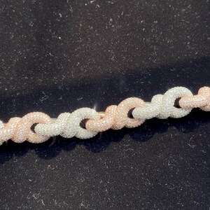 Peut inclure: Gros plan sur un collier cha&icirc;ne en argent et or rose. La cha&icirc;ne est compos&eacute;e de maillons entrelac&eacute;s, avec des segments argent&eacute;s et or rose altern&eacute;s. Le collier est pr&eacute;sent&eacute; sur un fond noir.