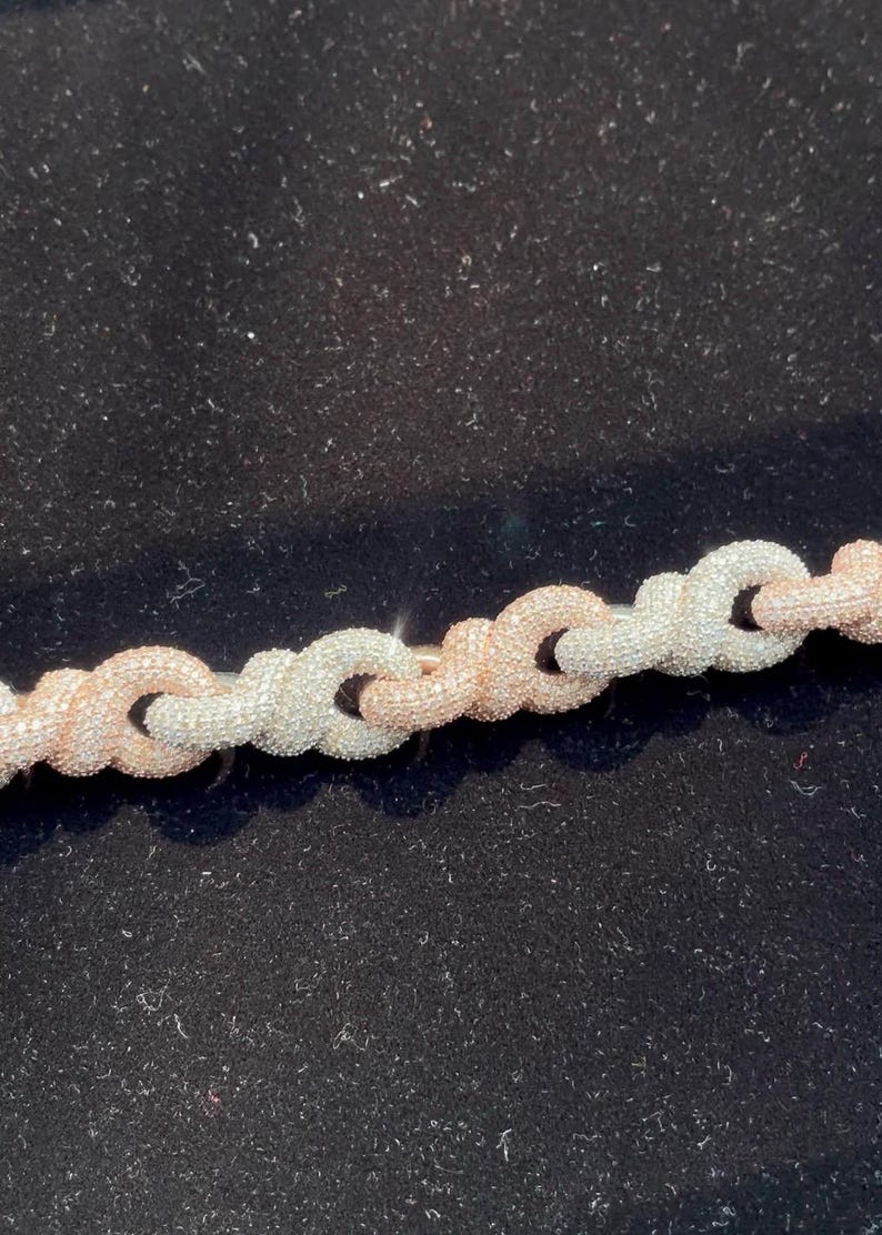 Peut inclure: Gros plan sur un collier cha&icirc;ne en argent et or rose. La cha&icirc;ne est compos&eacute;e de maillons entrelac&eacute;s, avec des segments argent&eacute;s et or rose altern&eacute;s. Le collier est pr&eacute;sent&eacute; sur un fond noir.
