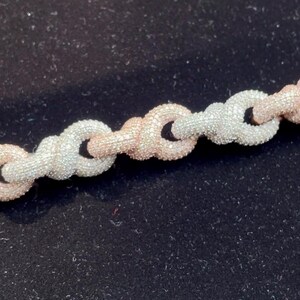 Peut inclure: Gros plan sur un collier cha&icirc;ne avec des maillons argent&eacute;s et or rose altern&eacute;s. Les maillons sont textur&eacute;s, donnant un aspect scintillant. Le bijou est pr&eacute;sent&eacute; sur un fond sombre.