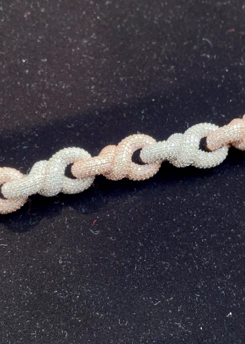 Peut inclure: Gros plan sur un collier cha&icirc;ne avec des maillons argent&eacute;s et or rose altern&eacute;s. Les maillons sont textur&eacute;s, donnant un aspect scintillant. Le bijou est pr&eacute;sent&eacute; sur un fond sombre.