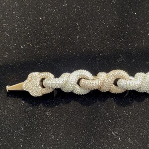 Peut inclure: Un bracelet en or et diamants avec un motif de cha&icirc;ne. Le bracelet pr&eacute;sente une s&eacute;rie de maillons interconnect&eacute;s, chacun incrust&eacute; de petits diamants &eacute;tincelants. Le fermoir est en or et &eacute;galement orn&eacute; de diamants. Le bracelet est pr&eacute;sent&eacute; sur une surface noire.