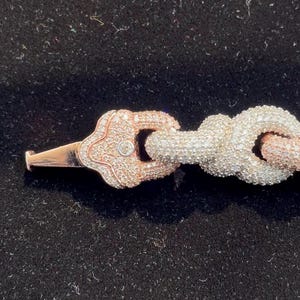 Peut inclure: Gros plan sur un bracelet en or rose et argent. Le bracelet est dot&eacute; d'un fermoir d&eacute;coratif avec un petit diamant et un motif de n&oelig;ud. Le bracelet est pos&eacute; sur un fond noir.