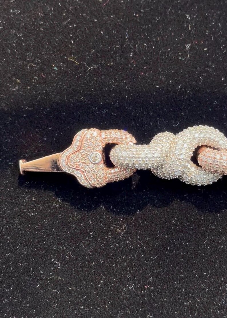 Peut inclure: Gros plan sur un bracelet en or rose et argent. Le bracelet est dot&eacute; d'un fermoir d&eacute;coratif avec un petit diamant et un motif de n&oelig;ud. Le bracelet est pos&eacute; sur un fond noir.