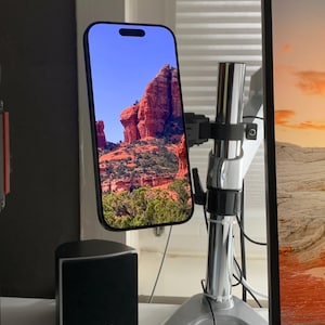 Könnte beinhalten: Ein schwarzes Smartphone, das eine Landschaft mit roten Felsformationen und grüner Vegetation zeigt, montiert auf einem silbernen und schwarzen verstellbaren Ständer. Ein schwarzer Lautsprecher mit dem Text "Teufel" ist sichtbar.