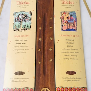 May include: Two incense sticks with packaging. The packaging is cream colored with brown text and illustrations. The incense sticks are brown and have a peace sign on the wooden holder. The text on the packaging reads "Triloka original herbal incense" and the scents are "hopi pinion" and "cinnamon spice".