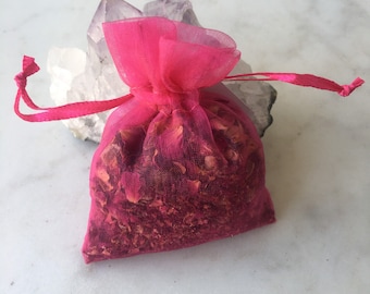 May include: A pink mesh bag filled with dried rose petals, sitting on top of a pile of white and purple crystals.