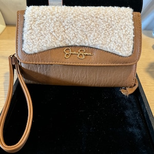 May include: A brown leather wallet with a white faux fur flap. The wallet has a gold metal logo that says "Jessica Simpson".
