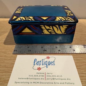 May include: A rectangular blue ceramic box with a lid, featuring decorative patterns in yellow, red, and black. The box is approximately 4 inches long. The business card of "Funtiques" is in the foreground, specializing in MCM decorative arts and pottery.