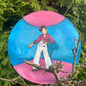 May include: A circular painting featuring a stylized figure with curly dark hair, wearing a magenta long-sleeve shirt and high-waisted white trousers with gold buttons. The background consists of a blue sky area above a pink ground surface.
