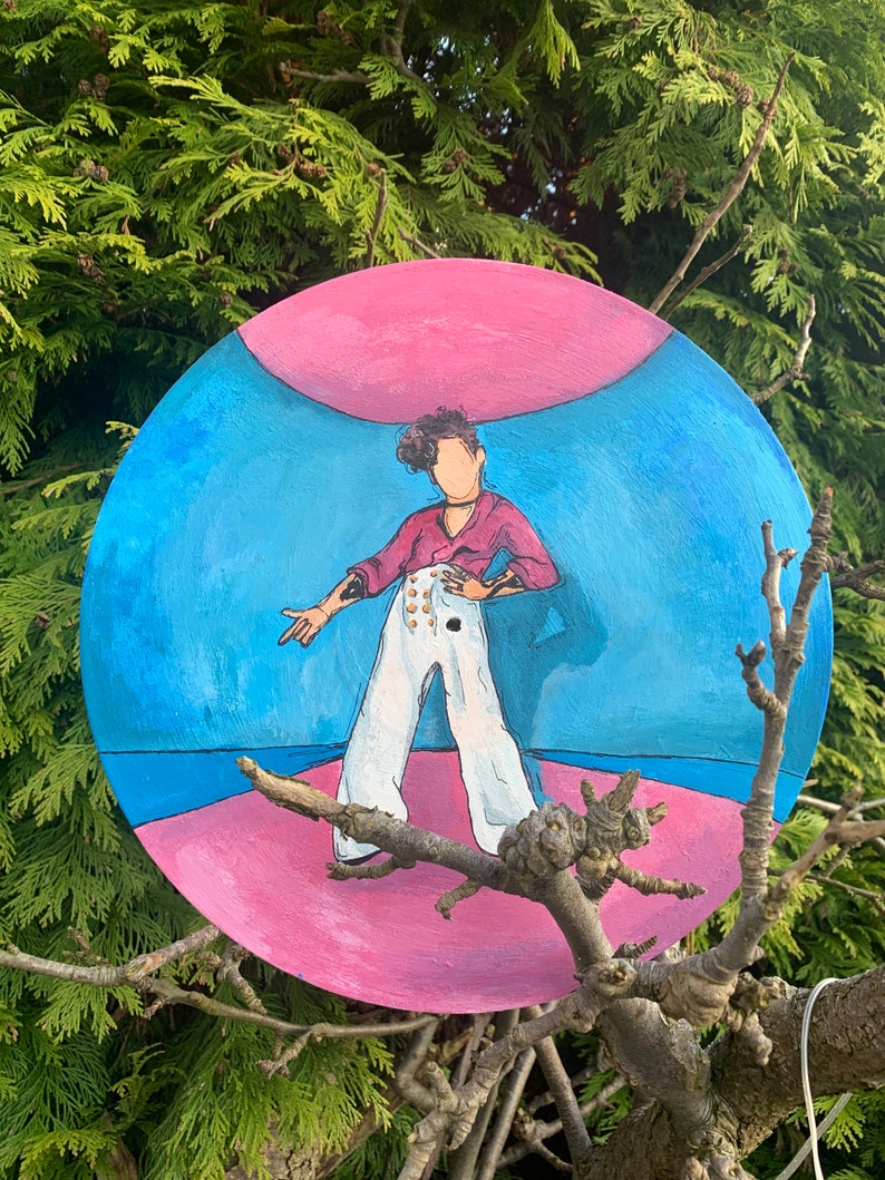 May include: A circular painting featuring a stylized figure with curly dark hair, wearing a magenta long-sleeve shirt and high-waisted white trousers with gold buttons. The background consists of a blue sky area above a pink ground surface.