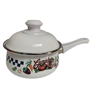 May include: White enamel saucepan with lid. The pot features a handle and is decorated with a Campbell's logo and colorful illustrations of vegetables. A blue and white checkered pattern adorns the pot's exterior.