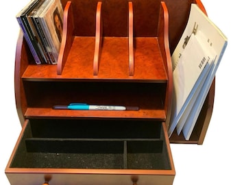 May include: A wooden desk organizer with a rich, reddish-brown finish. It features multiple compartments for storage, including slots for CDs and files, a drawer, and a shelf. A blue and black Sharpie pen rests on the shelf.