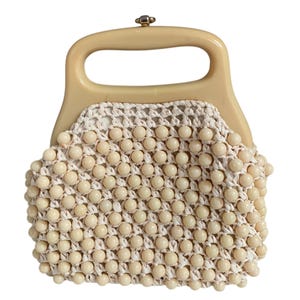 May include: A cream-colored handbag featuring a structured, smooth plastic handle and a body crafted from woven off-white cord embellished with numerous round, matching cream-colored beads throughout the entire exterior surface of the bag.